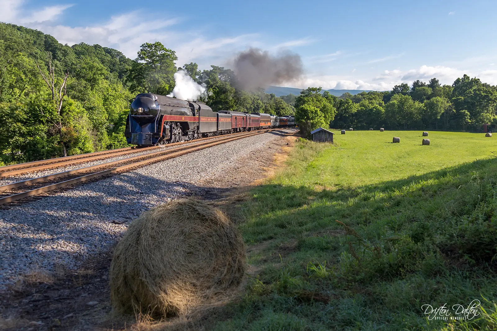 Steam locomotive pulling passenger cars past a green field