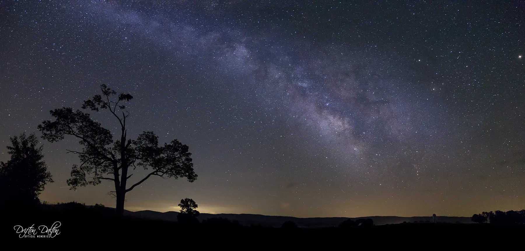 Milky Way arching above silhouetted trees and a distant Appalachian horizon