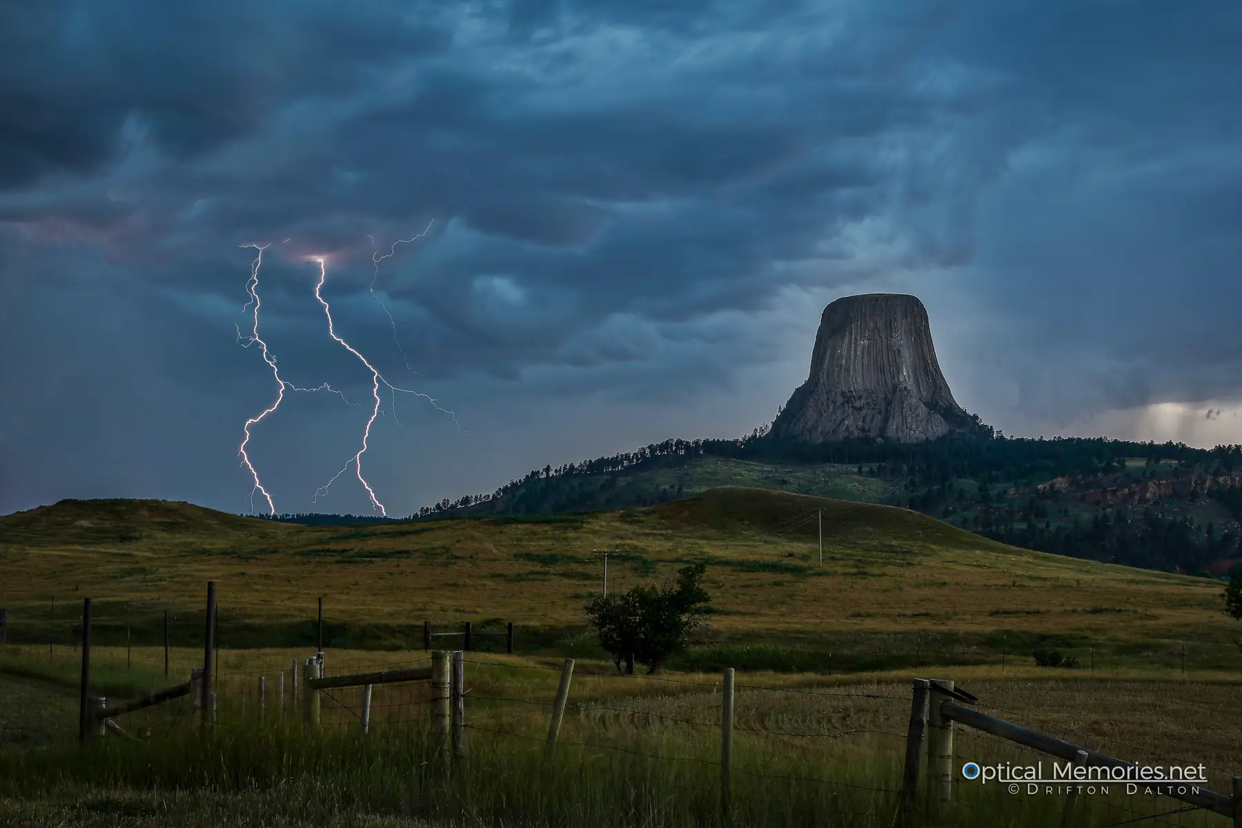 Multiple lightning bolts striking behind Devils Tower beneath dark storm clouds