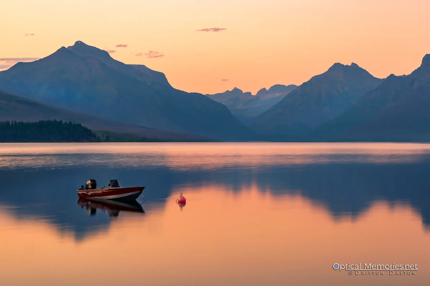 Small boat resting on Lake McDonald beneath mountains in warm sunset light