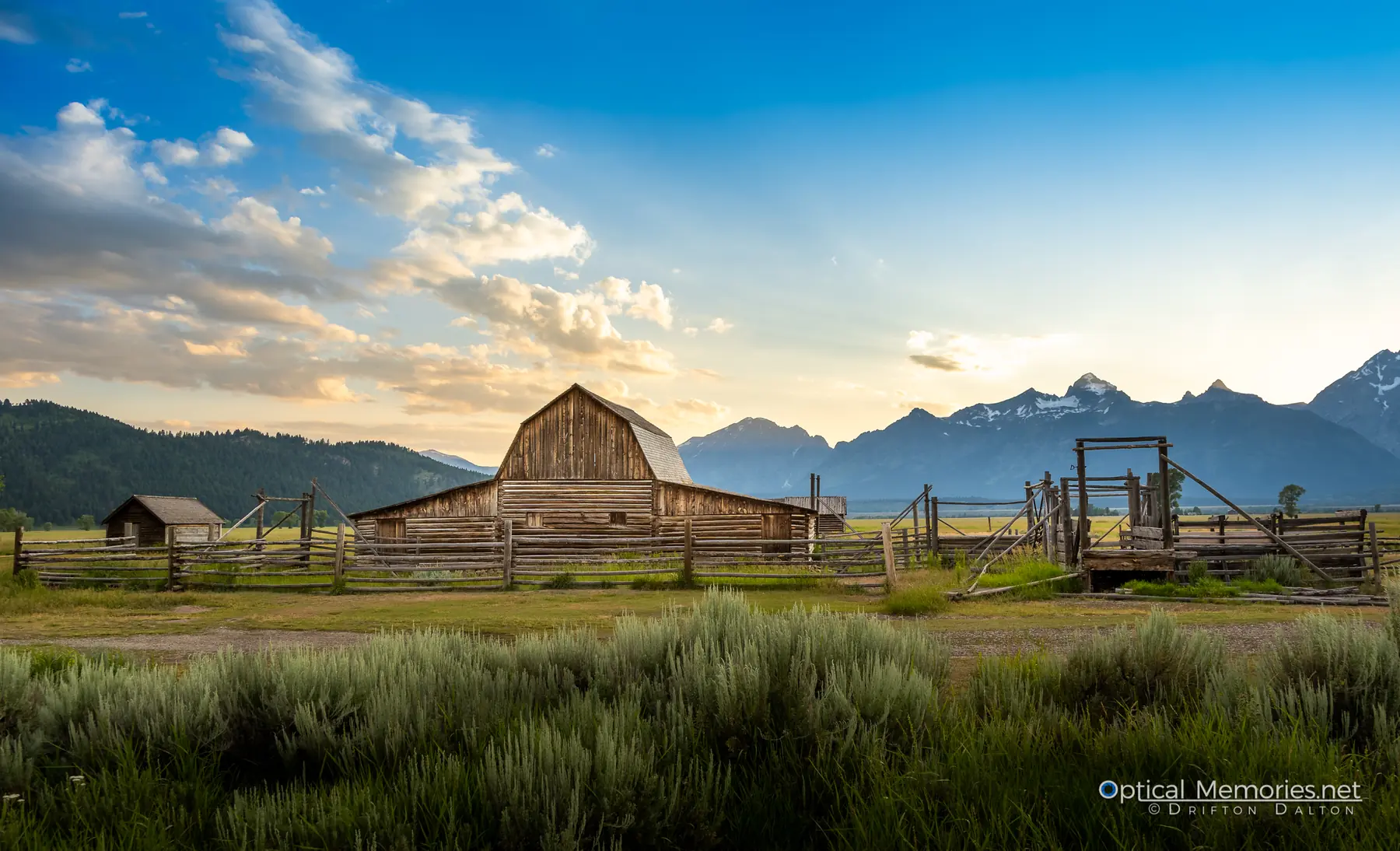 Wide view of a historic Moulton barn, fences, grassland, and the Teton Range